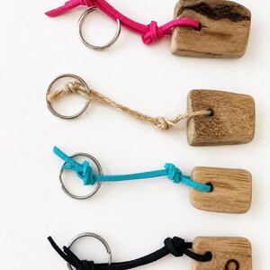 Pu&ograve; includere: Quattro portachiavi con pezzi rettangolari di legno naturale dalle texture variegate. Ogni pezzo &egrave; fissato a un anello metallico argentato tramite un cordino. I cordini sono rosa acceso, beige, turchese e nero, ciascuno con nodi semplici.