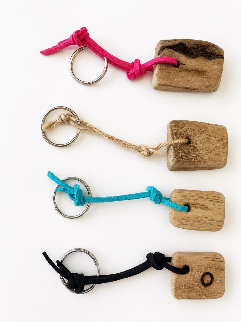 Pu&ograve; includere: Quattro portachiavi con pezzi rettangolari di legno naturale dalle texture variegate. Ogni pezzo &egrave; fissato a un anello metallico argentato tramite un cordino. I cordini sono rosa acceso, beige, turchese e nero, ciascuno con nodi semplici.