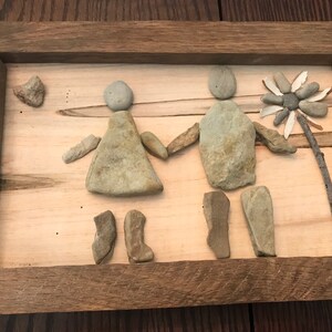 Puede incluir: Una obra de arte enmarcada hecha con piedras que representa a una pareja tomándose de la mano con una flor en el fondo.