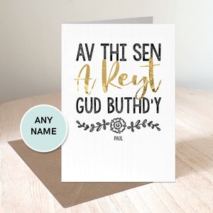 May include: A white card with black text that reads "Av thi sen a reyst gud buthd'y" with a gold foil accent on the word "reyst". The card has a small black floral design with the name "Paul" underneath.