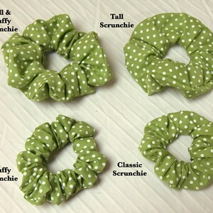 Op de afbeelding: Vier groene scrunchies met witte stippen. De scrunchies zijn gerangschikt in twee rijen van twee. De scrunchie linksboven is gelabeld "Tall & Fluffy Scrunchie", de scrunchie rechtsboven is gelabeld "Tall Scrunchie", de scrunchie linksonder is gelabeld "Fluffy Scrunchie", en de scrunchie rechtsonder is gelabeld "Classic Scrunchie".