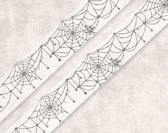 May include: A white ribbon featuring a repeating pattern of black spiderwebs and small spiders. The design includes delicate, dangling beaded accents hanging from the web structures, creating a continuous decorative border across the fabric surface.