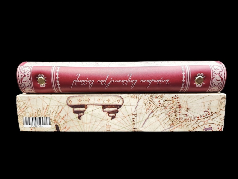 May include: A red leather-bound journal with the words "planning and journaling companion" embossed on the cover. The journal is sitting on a box with a vintage map design.