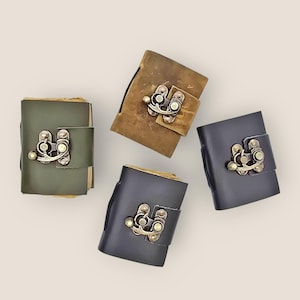 May include: Four small leather journals in shades of green, brown, and grey. Each journal has a metal clasp closure. The journals are arranged on a neutral background.