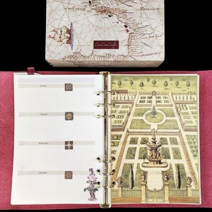 May include: A red felt-covered binder with a white interior. The interior has a weekly planner layout with a decorative garden illustration on the right page. The illustration features a fountain and a variety of plants and trees.