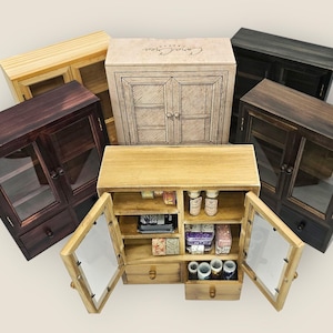 May include: A selection of small wooden cabinets in different finishes: natural, dark brown, black, and a boxed cabinet. The cabinets feature glass doors, drawers, and shelves, some with contents visible. The open cabinet displays small items.