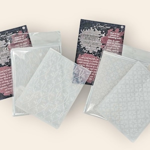 Könnte beinhalten: Mehrere Prägeordner mit floralen Mustern werden gezeigt. Jeder Ordner ist in einer transparenten Kunststoffhülle verpackt. Die Verpackung enthält ein schwarz-graues Etikett mit der Aufschrift "Embossing Folder Floral Pattern".