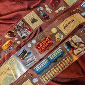 Puede incluir: Pegatinas decorativas con temas de viajes vintage. Incluye imágenes de un tren, mapas, billetes, un reloj de bolsillo y las palabras "Orient Express" y "Daily News". Las pegatinas están sobre un fondo transparente.