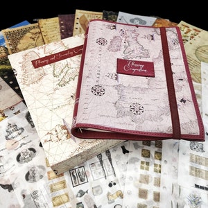 May include: A red leather-bound journal with a map design and the text "Planning Expedition" on the cover. The journal is surrounded by various decorative papers, stickers, and ephemera, including a compass, butterflies, and a castle.