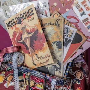 Puede incluir: Una colección de efímeras de temática vintage, que incluye postales, pegatinas y cintas decorativas. El punto focal es un póster de "Moulin Rouge Paris". Otros artículos incluyen una pequeña lata con el texto "The New Look" y varias ilustraciones retro.
