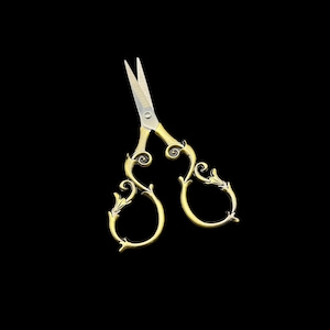 May include: Gold-toned embroidery scissors with ornate, swirling handles and sharp, silver blades. The scissors have a classic design with decorative flourishes, set against a black background. Ideal for sewing and crafting.