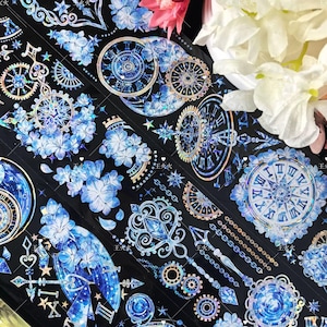 May include: Decorative washi tape featuring a repeating pattern of clocks, gears, flowers, and celestial elements in shades of blue and silver against a black background. The tape has a holographic, iridescent finish, adding a shimmering effect.