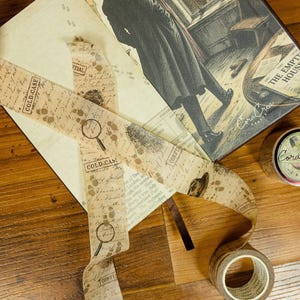 May include: A book titled The Empty House featuring an illustration of a person in a long coat looking out a window, accompanied by a roll of decorative tape printed with magnifying glasses, footprints, fingerprints, and the text Cold Case.