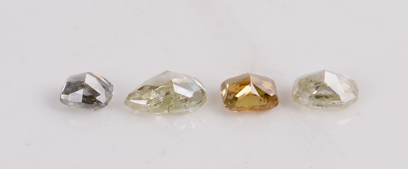 Puede incluir: Cuatro diamantes sueltos de diferentes tama&ntilde;os y colores. Los diamantes est&aacute;n cortados en una forma &uacute;nica y facetada. Los diamantes est&aacute;n dispuestos en una fila de izquierda a derecha, con el diamante m&aacute;s peque&ntilde;o a la izquierda y el diamante m&aacute;s grande a la derecha. Los diamantes son todos transparentes, pero tienen diferentes tonos de gris, verde y marr&oacute;n.