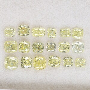 Op de afbeelding: Een verzameling van 16 kussen geslepen gele diamanten, gepresenteerd op een wit oppervlak. De diamanten zijn gerangschikt in vier rijen van vier.