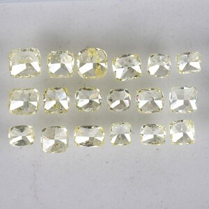 Op de afbeelding: Een verzameling van 16 kussen geslepen gele diamanten, gerangschikt in rijen op een wit oppervlak.