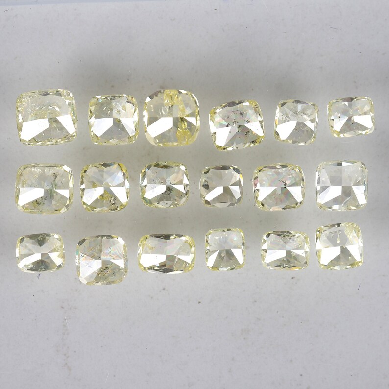 Op de afbeelding: Een verzameling van 16 kussen geslepen gele diamanten, gerangschikt in rijen op een wit oppervlak.