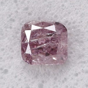 Puede incluir: Un diamante rosa de talla cojín. El diamante está facetado y tiene un ligero tono púrpura.