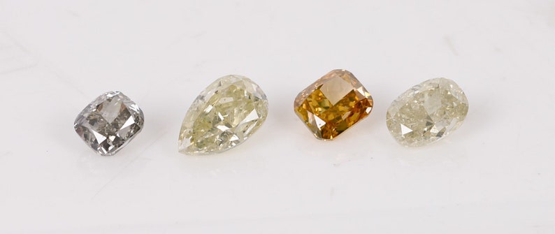 Puede incluir: Cuatro diamantes sueltos de diferentes formas y colores. Los diamantes son gris claro, amarillo claro, marr&oacute;n claro y blanco claro.