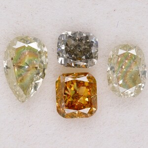 Puede incluir: Cuatro diamantes sueltos de diferentes formas y colores. Un diamante de forma pera, un diamante cuadrado de talla coj&iacute;n, un diamante redondo brillante y un diamante cuadrado de talla esmeralda. Los diamantes est&aacute;n todos sobre un fondo blanco.