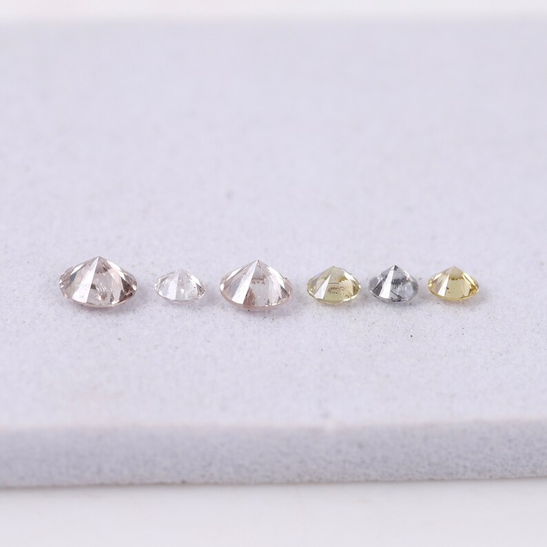 K&ouml;nnte beinhalten: Sechs runde, facettierte Diamanten in verschiedenen Gr&ouml;&szlig;en und Farben, darunter Braun, Wei&szlig;, Gelb und Grau, in einer Reihe auf einer wei&szlig;en Oberfl&auml;che angeordnet.