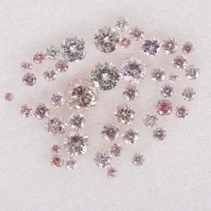 Puede incluir: Una colección de diamantes sueltos de color rosa y blanco de varios tamaños, expuestos sobre una superficie blanca.