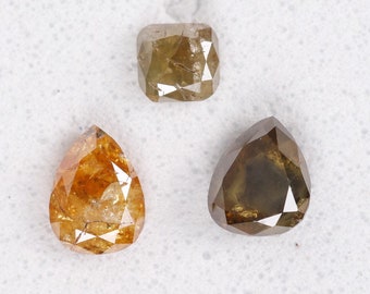 May include: Three loose, faceted diamonds in shades of brown and yellow. The shapes include a cushion cut, a pear shape, and a second pear shape. The diamonds are set against a white background.