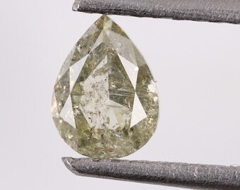 Puede incluir: Un diamante de forma de pera, de color verde claro, con un corte facetado. El diamante está sujeto por unas pinzas.