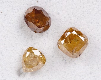 May include: Three brown and yellow rough cut diamonds of different shapes. The diamonds are on a white background.