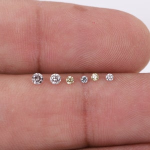K&ouml;nnte beinhalten: Nahaufnahme von sieben kleinen runden Diamanten, einige sind klar und einige sind gelb, auf einem Finger.
