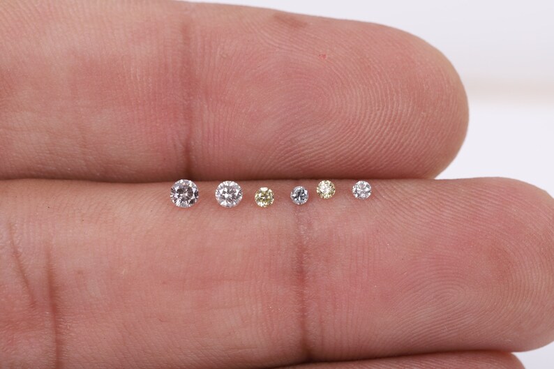 K&ouml;nnte beinhalten: Nahaufnahme von sieben kleinen runden Diamanten, einige sind klar und einige sind gelb, auf einem Finger.