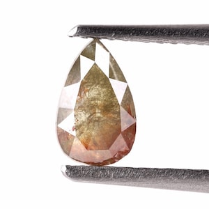 May include: A pear-shaped, raw diamond with a brown and green colour. The diamond is held by a pair of tweezers.