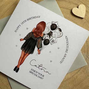 May include: A white card with a black and silver illustration of a woman holding balloons that say "18". The card says "Happy 18th Birthday" and "Catrin" with the text "Enjoy your special day!" below.