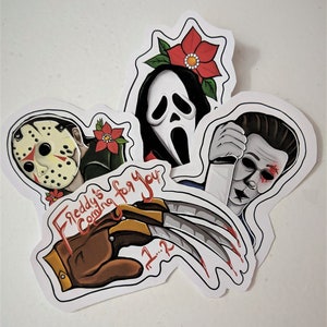 K&ouml;nnte beinhalten: Vier Horrorfilm-Charakter-Aufkleber. Die Aufkleber zeigen Freddy Kruegers Handschuh, Jason Voorhees' Maske, Ghostface und Michael Myers. Die Aufkleber sind wei&szlig; mit schwarzen Umrissen und roten und gr&uuml;nen Akzenten.