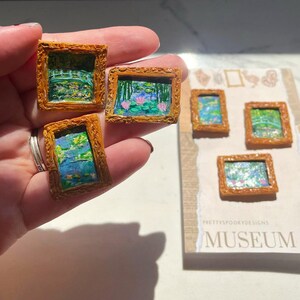 May include: Five miniature framed paintings of water lilies and bridges, with a gold frame and a white background. The paintings are labelled "MUSEUM" on the bottom.
