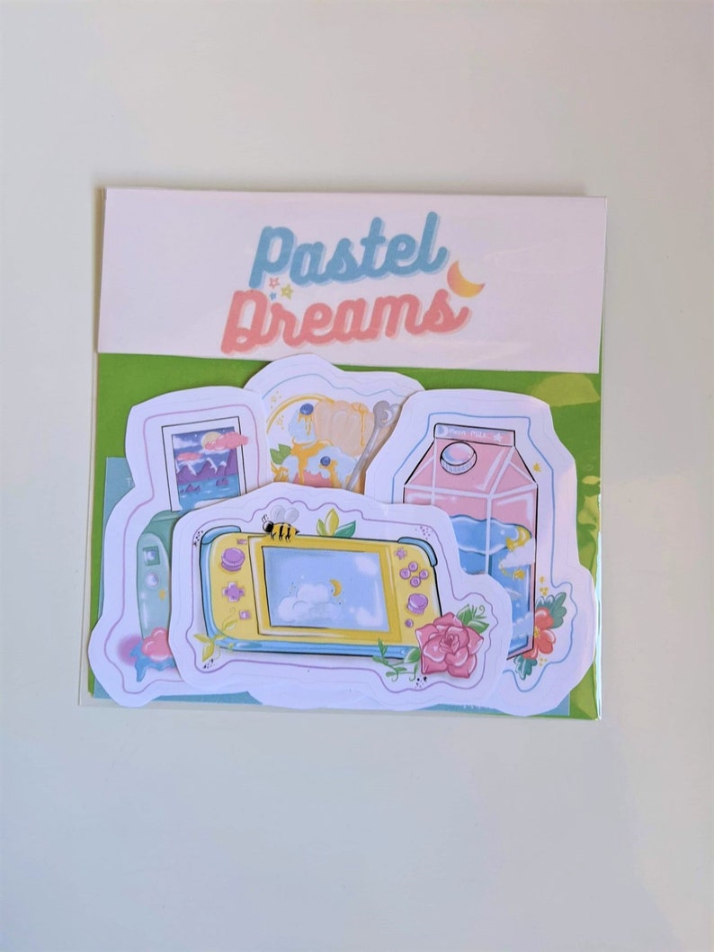 May include: A set of four pastel-colored stickers featuring a video game console, a milk carton, a night sky scene, and a floral design. The stickers are on a white background with the text "Pastel Dreams" in blue and pink.