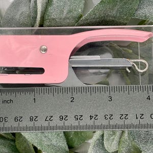 May include: A pink mini stapler in a clear plastic case, next to a ruler. The stapler is approximately 4 inches long. The ruler shows measurements in inches and numbers from 0 to 30.
