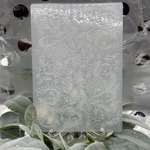 Pode incluir: Um molde retangular transparente com um design floral em relevo com folhas e bagas. O molde é feito de um material translúcido e é adequado para artesanato ou fins decorativos. O design é intrincado e detalhado, com uma estética vintage.