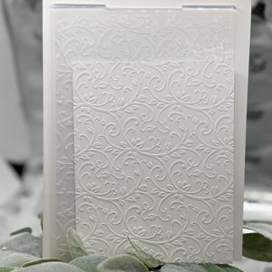 Op de afbeelding: Een transparante embossing folder met een gedetailleerd, verhoogd bloemen- en wijnstokpatroon. Het ontwerp is een herhalend, wervelend motief van bladeren en stelen. De map is gemaakt van transparant plastic en is ontworpen voor papierknutsel- en scrapbookingprojecten.