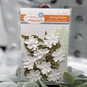 May include: A package of white paper flowers and green leaves for crafting. The package reads "Spring Kisses" and "Fun Stampers Journey". The package contains 24 pieces, including 16 flowers and 8 leaves.