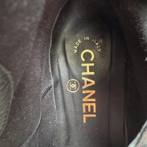 May include: Interior view of a black boot with a leather insole. The insole features the gold-colored text "CHANEL" and the Chanel logo. The text "MADE IN ITALY" is also visible.