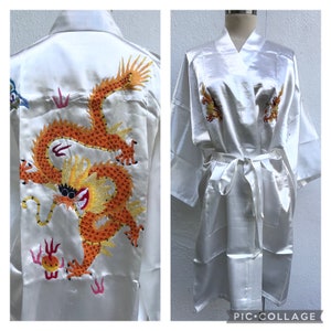 May include: White satin robe with an embroidered orange dragon on the back. The robe has a tie belt and long sleeves.