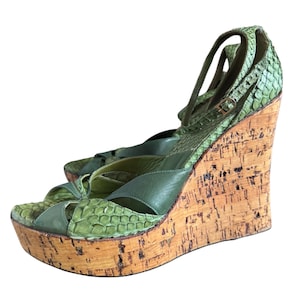 May include: Green wedge sandals with a snakeskin pattern on the straps and toe. The platform and wedge heel are made of cork. The sandals have an ankle strap with a buckle.