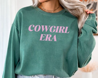 May include: A light green sweatshirt with the text "COWGIRL ERA" in pink lettering.