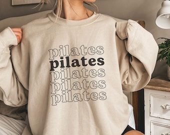 May include: A beige sweatshirt with the word "pilates" repeated five times in black text.
