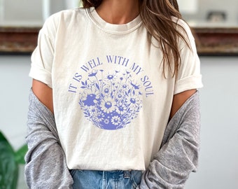 May include: A white t-shirt with a purple floral design and the text "It is well with my soul".