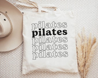 May include: A white tote bag with black text that reads "pilates" five times, stacked on top of each other.