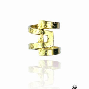 Op de afbeelding: Gouden ring met een geometrisch ontwerp. De ring is gemaakt van gehamerd metaal en heeft een textuur.