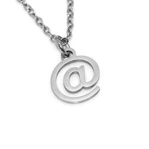 Puede incluir: Un collar de plata con un colgante en forma de arroba.