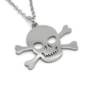 Peut inclure: Un collier avec un pendentif en forme de crâne et d'os croisés en argent. Le pendentif est en métal et présente un design détaillé.